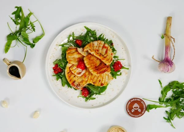 На тарелку для подачи выложить рукколу и обжаренные кальмары. Оформить соусом, посыпать кунжутом. Приятного аппетита!
