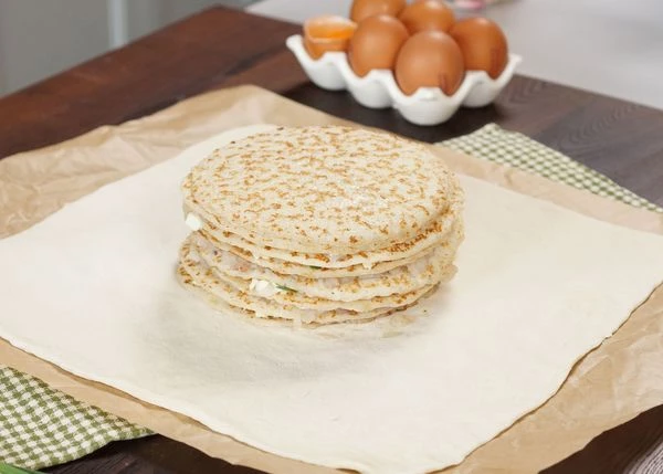 Тесто разморозить на нижней полке холодильника. Раскатать до толщины 3 мм. Выложить на пергамент. На тесто переложить заготовку с блинчиками. 