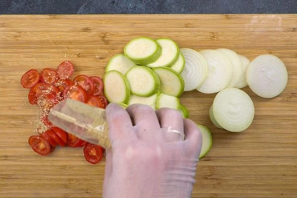 Лук нарезать кольцами, кабачок и помидоры кругляшами, посыпать специями.