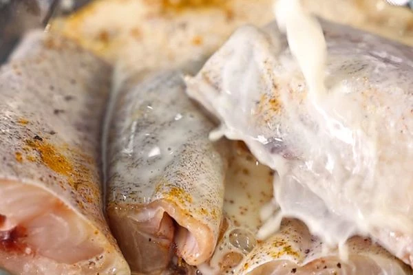 Нарезанный минтай переложить в миску, посолить, поперчить, добавить куркуму и влить молоко. 