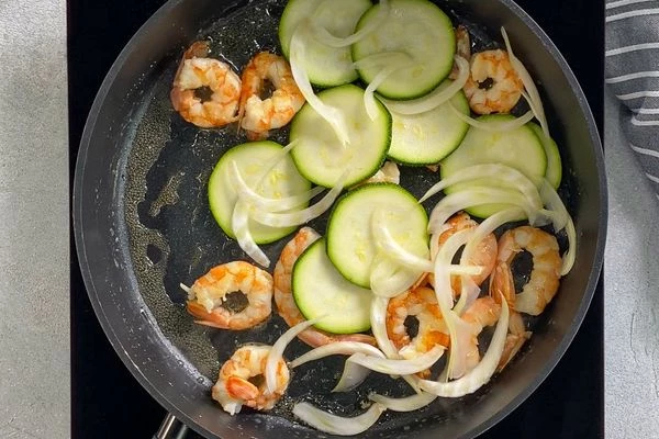 Цукини и фенхель вымыть, нарезать слайсами. Затем выложить цукини и фенхель к креветкам, жарить еще минуту, периодически помешивая.