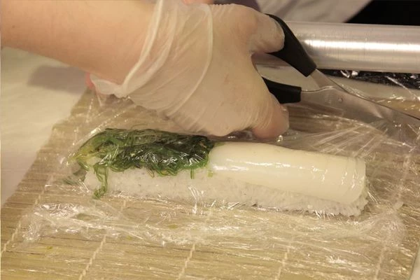 В центр нори положить полоску сыра, рядом перо зеленого лука. Свернуть ролл рисом наружу.