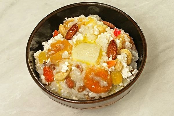 Переложить готовую кашу в тарелку, в центр выложить творог,  украсить орешками, цукатами и кусочком сливочного масла.