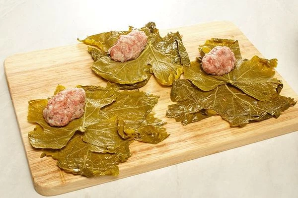 На доске разложить виноградные листья. С краю на лист положить небольшой колобок фарша.