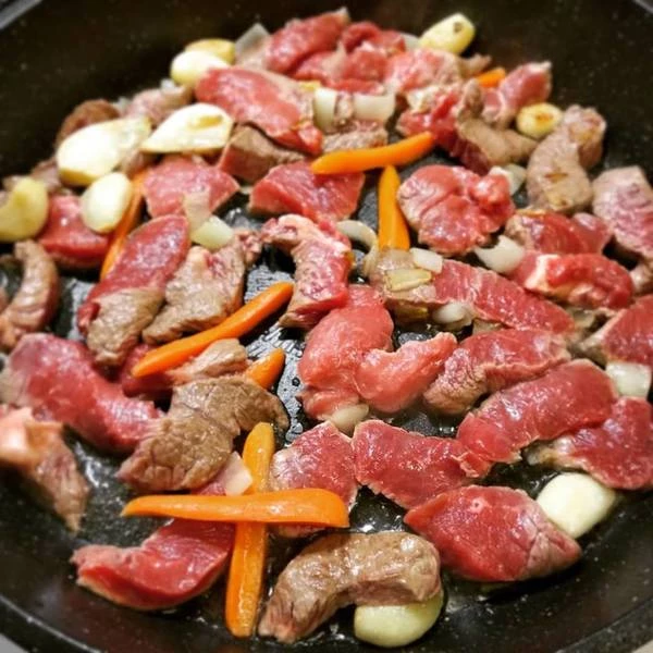 Добавить мясо и морковь, хорошо перемешать и добавить воду. Накрыть крышкой и потушить примерно 10 минут.