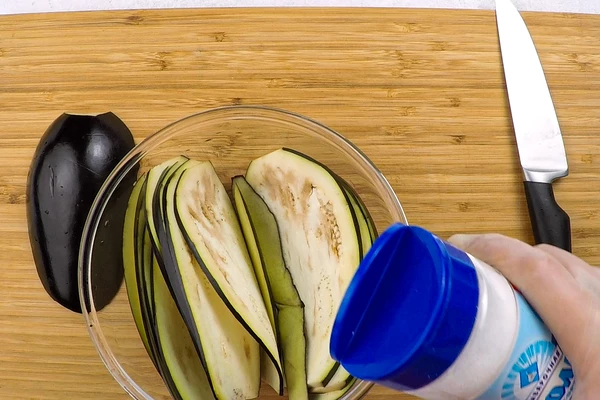  Баклажаны нарезать тонкими пластиками. Если овощ крупный, то разрезать вдоль пополам. Посыпать солью и оставить на 15 минут, потом промыть под проточной водой. (Если баклажаны молодые, то солью можно не посыпать.)