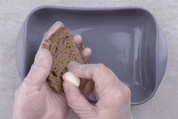 Хлеб нарезать пластиками толщиной 1-1,5см, натереть чесноком или выложить раздавленный чеснок сверху. Поставить в духовку подсушиться минут на 10-15 при температуре 150-160С.