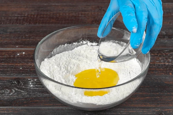 В глубокой чашке смешать муку пшеничную и рисовую, добавить сахар, перемешать. Затем добавить 1 яйцо и воду, замесить тесто, накрыть и оставить на 15-20 минут.