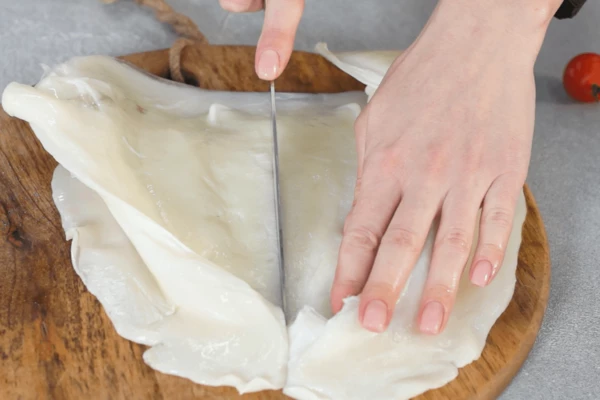 Каракатицу разморозить на нижней полке холодильника, очистить от пленок, отделить голову от тушки, тушку разрезать пополам.