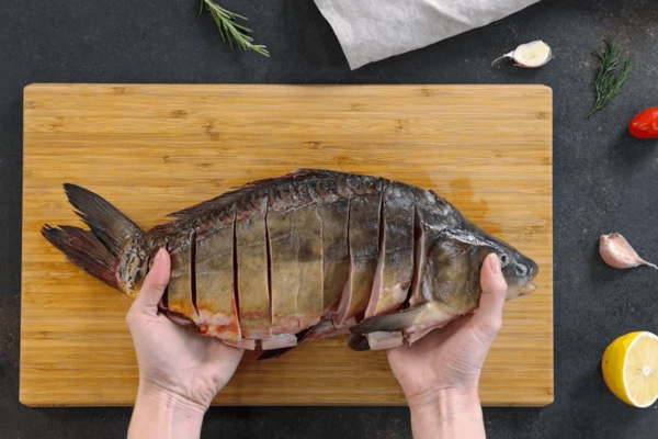 Карпа вымыть, выпотрошить и снова вымыть. Потрошить надо аккуратно, чтобы не повредить желчный пузырь.
Затем с каждой стороны рыбы сделать поперечные надрезы по 2-3 см, не задевая хребет. 
