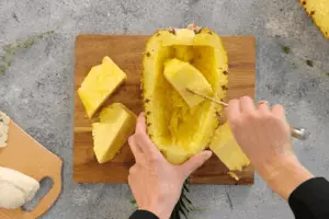 Ананас вымыть, обсушить полотенцем. Разрезать вдоль пополам. Ножом аккуратно подрезать мякоть внутри ананаса, оставляя стенки, толщиной ~ 8 - 10 мм.