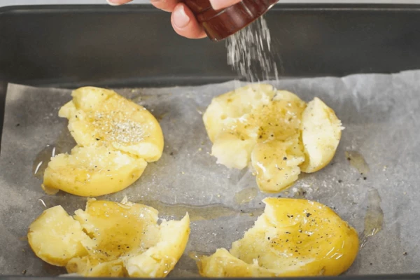 Картофель вымыть, отварить в подсоленной воде до полуготовности, воду слить. На противень с пергаментом налить немного масла, выложить картофель и примять, придав форму лепешки толщиной 0,5 см. Посолить и поперчить. 