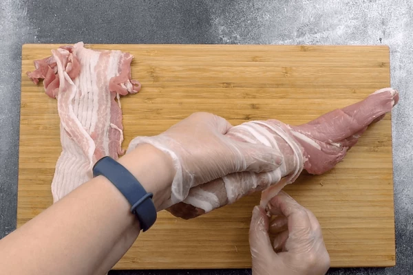 Свиную вырезку обернуть полосками бекона.