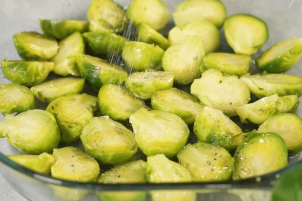 Брюссельскую капусту разморозить на нижней полке холодильника. Порезать ее на половинки, переложить в форму для запекания, посолить, поперчить, сбрызнуть оливковым маслом.