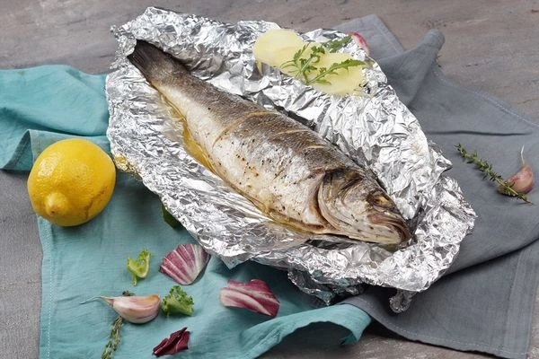 Готового сибаса украсить свежими овощами и дольками лимона.