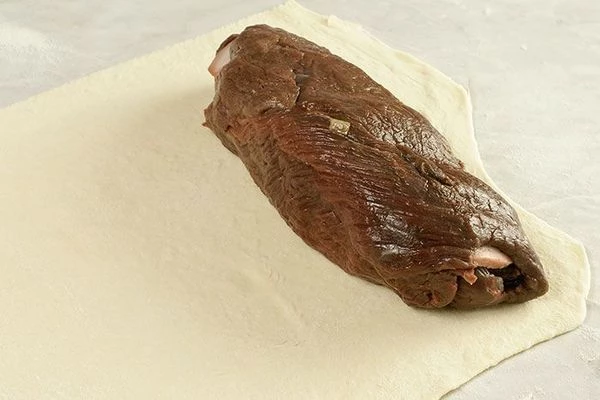 С краю на тесто положить рулет из оленины.