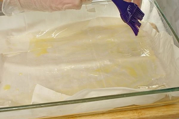 В это время подготовить тесто фило: в смазанную сливочным маслом форму выложить первый лист теста, промазать растопленным маслом, сверху выложить еще лист теста.  Укладывать так, смазывая, 4-5 листов.