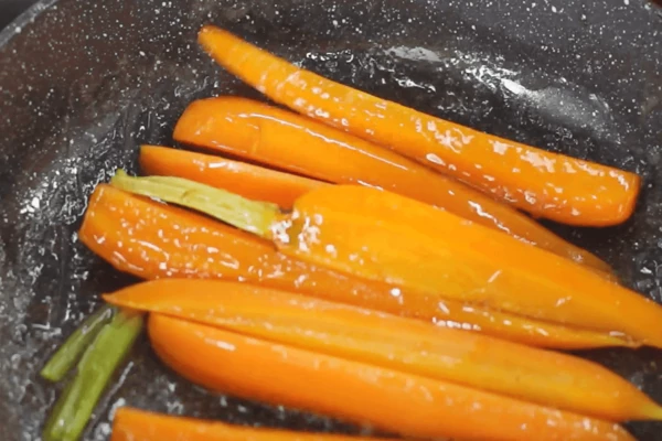 Уменьшить нагрев и выложить на сковороду подготовленную морковь. Обжаривать 4- 5 минут на среднем огне, помешивая, чтобы морковь равномерно покрылась глазурью.