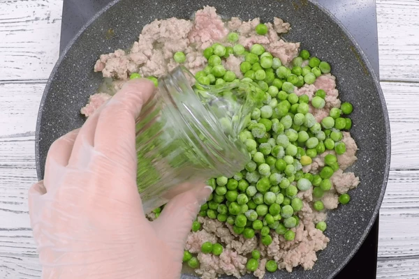 На этой же сковороде обжарить фарш 3-4 минуты, добавить зеленый горошек и воду, потушить 3-4 минуты, посолить, поперчить. 
