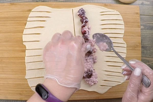 Готовое тесто разделить на 6-8 частей, сформовать шарики. Затем каждый шар тонко раскатать прямоугольной формы, разрезать на две части. С одной стороны выложить начинку, с другой стороны сделать надрезы-полоски.