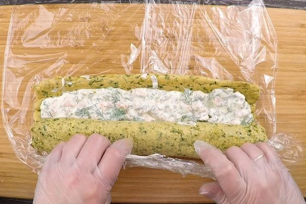 Подготовленное рулетное тесто освободить от пергамента, выложить начинку, плотно завернуть, с помощью пищевой пленки. Оставить на 1-2 часа в холодильнике.
