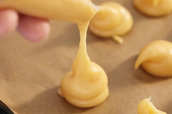 Переложить в кондитерский мешок. Отсадить тесто на противень с пергаментом.