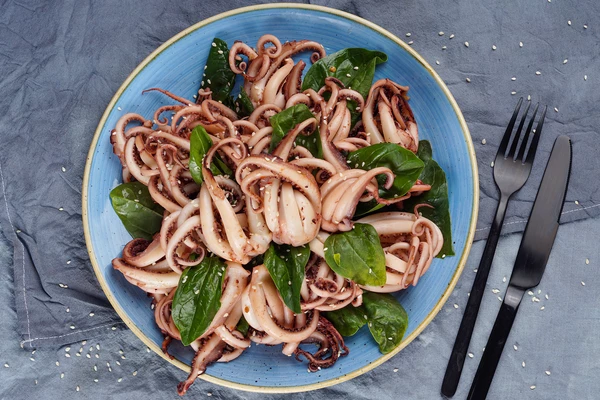 Листья шпината нарвать на крупные части, сверху выложить готовые щупальца кальмара.