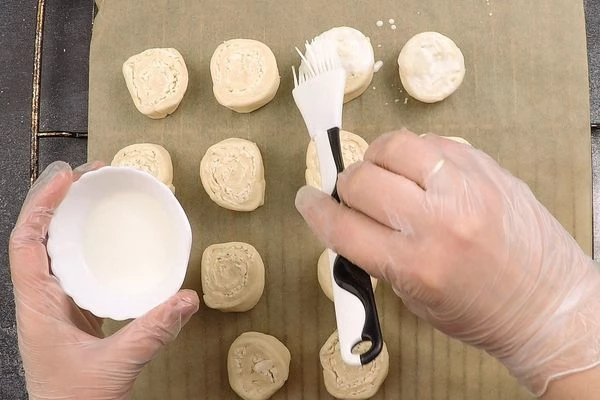  Переложить булочки разрезом вверх на пергамент, смазать кефиром (можно взять сметану). 