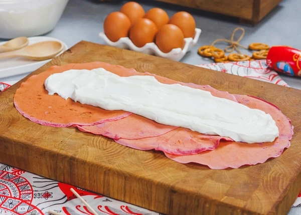 На доску выложить блинчики испеченной стороной вверх внахлест. На ⅓ часть выложить начинку.