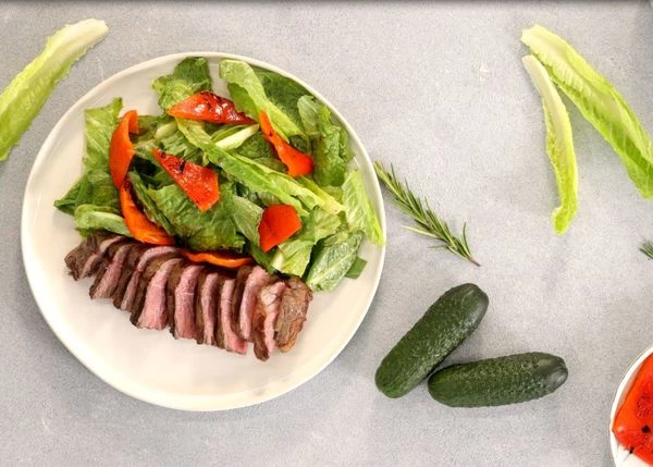 На тарелку для подачи выложить листья салата, рядом нарезанный стейк. Оформить нарезанным перцем и огурцом. Приятного аппетита!