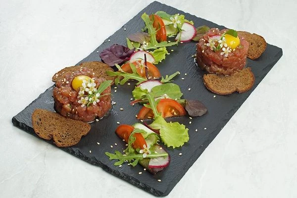 В центре тартара сделать небольшое углубление, выложить желток перепелиного яйца. Украсить салатом из свежих овощей, сбрызнуть заправкой. Подавать с тонкими гренками.