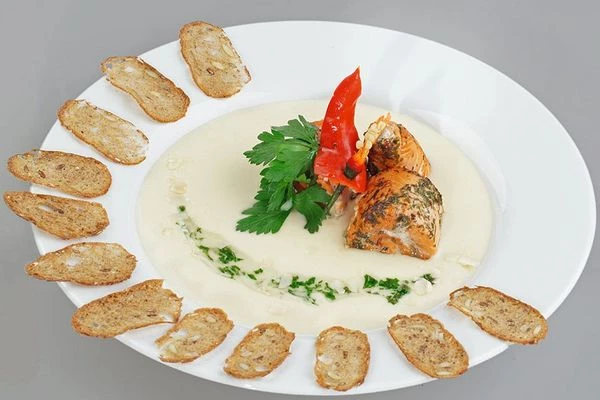 При подаче в тарелку налить кокосовый суп, сверху выложить рулетики из рыбы, украсить зеленью и гренками.