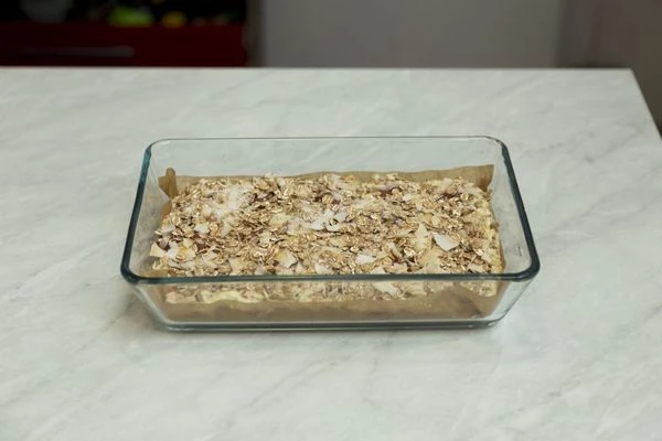 Приготовьте обсыпку: смешайте овсяные хлопья, сахар и кокосовые чипсы. Покройте ровным слоем обсыпки тесто.
