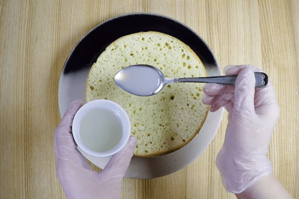 Выложить первый корж на тарелку, пропитать кокосовым сиропом. 