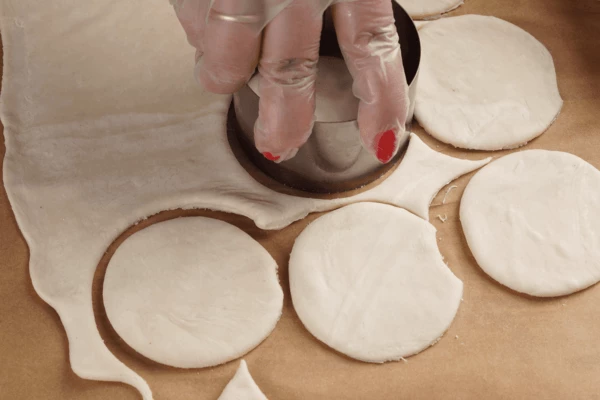 Тесто разморозить на нижней полке холодильника, немного раскатать. С помощью формы вырезать круги необходимого диаметра (у нас 7см).