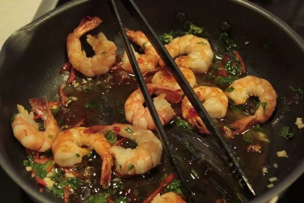 На разогретой сковороде с оставшимся сливочным маслом обжарить креветки 2-3 минуты, добавить рубленный чеснок, зелень, перец чили. Влить соус чили, выпарить 2-3 минуты. (не пережаривая креветки)