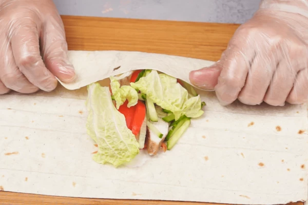 На лаваш выложить сметанный соус, морковь, помидоры, огурцы, готовую грудку и листья салата. Завернуть конвертиком. 