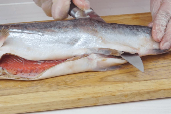Горбушу разморозить естественным способом на нижней полке холодильника, промыть под холодной водой, обсушить. Разрезать вдоль хребта на 2 филе. Срезать реберные кости. Филе снять острым ножом с кожи.