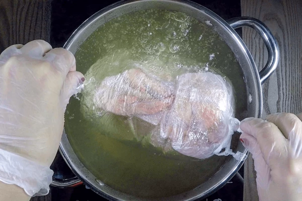 В глубокую кастрюлю налить воду (чтобы накрывало курицу), подсолить, довести до кипения. Положить курицу, луковицу, дольки моркови, перец горошком, можно добавить веточки зелени. Варить на среднем огне 90-100 минут (пленку наколоть в нескольких местах зубочисткой, чтобы курица пропиталась ароматным бульоном)