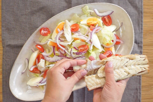  Салат айсберг нарвать крупными кубиками, выложить горкой на тарелку, сверху украсить яйцами, помидорами и луком, выложить кусочки подготовленной рыбы и полить заправкой.