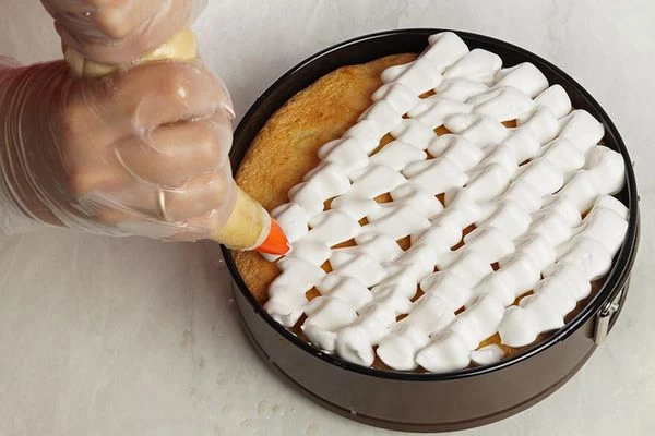 Шарлотку достать из духовки, быстро украсить кремом-безе. Поставить снова в духовку, снизив температуру до 130-140С на 20-25 минут. 