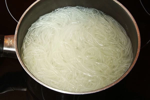 Отдельно сварить рисовую лапшу, опустив ее в кипящую воду на пару минут. Затем разложить по глубоким тарелкам.