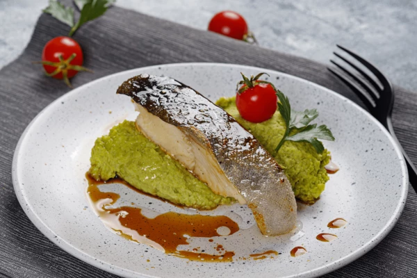 Пюре из горошка выложить горкой, сверху порцию готовой рыбы, украсить соусом терияки и помидором черри.