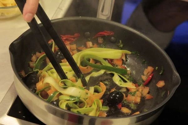 На разогретой сковороде с оливковым маслом обжарить чеснок, перец чили. Влить лимонный сок, добавить полоски моркови и цукини. Обжарить 1 минуту.