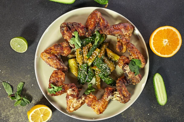 На блюдо для подачи выложить крылья и битые огурцы. Оформить листьями кинзы и кунжутом.