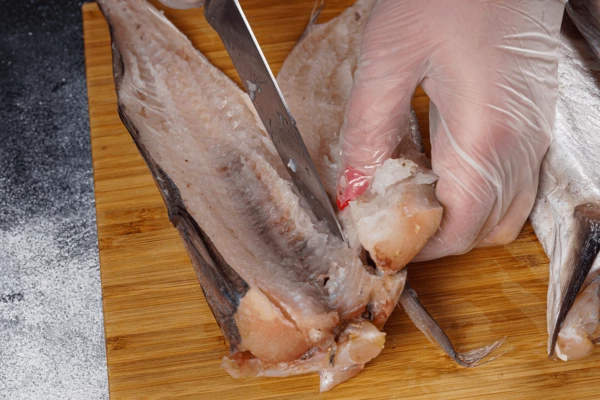 Пикшу разморозить естественным способом на нижней полке холодильника. Разрезать вдоль хребта на 2 части.