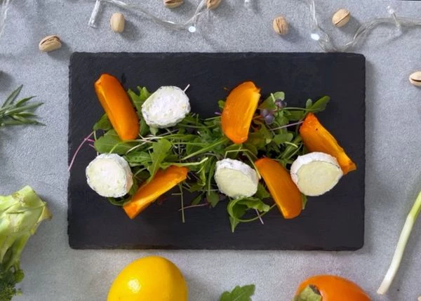 На тарелку выложить зелень, хурму и козий сыр. 
