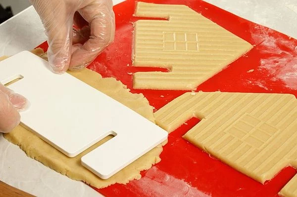   Раскатанное тесто вырезать по трафарету на силиконовом коврике или на пергаментной бумаге. В нижней части домика и стен нужно сделать прорези, чуть шире, чем толщина стен, чтобы удобнее было собирать.