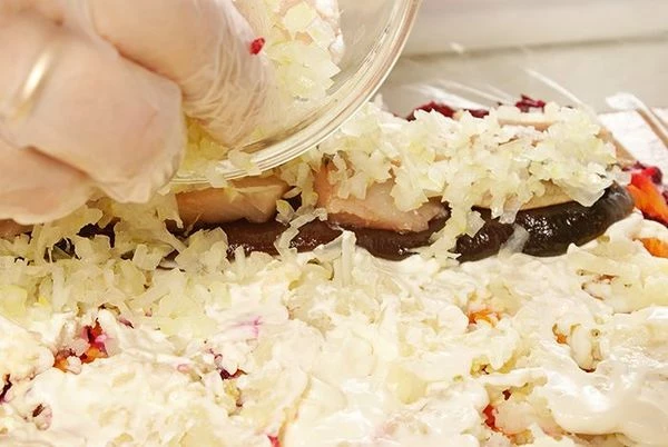 С самого края получившегося овощного прямоугольника выложить пластики селедки, накройте их сверху луком.