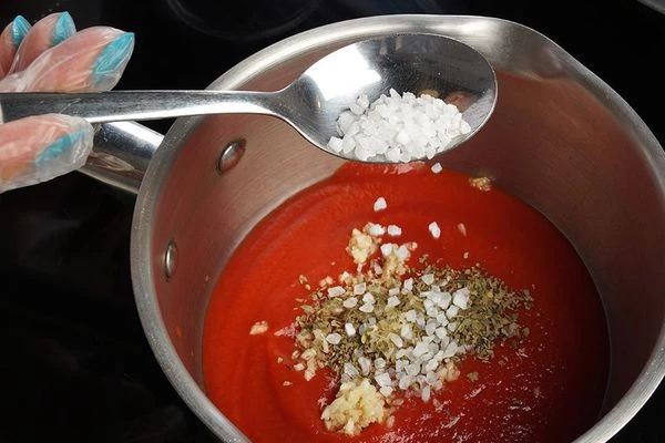 Томатный соус влить в небольшую кастрюльку, довести до вкуса солью, сахаром, чесноком и специями.